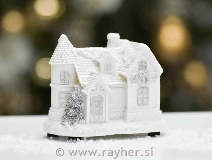 Zasnežena bela hiška z lučko in smreko